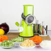 Manual rotary vegetable slicer with stainless steel drums next to sliced veggies on wooden cutting board.
