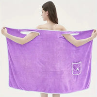 Adult wearing a purple wearable bath towel with bowknot design, featuring pockets and quick-drying coral velvet material.