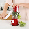 Manual rotary vegetable slicer in red with shredded zucchini being collected in a bowl, ideal kitchen gadget for home cooking.
